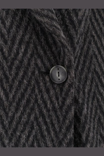 Black circular matte button embedded in dark gray herringbone wool fabric on hevò men’s santa cesarea coat
