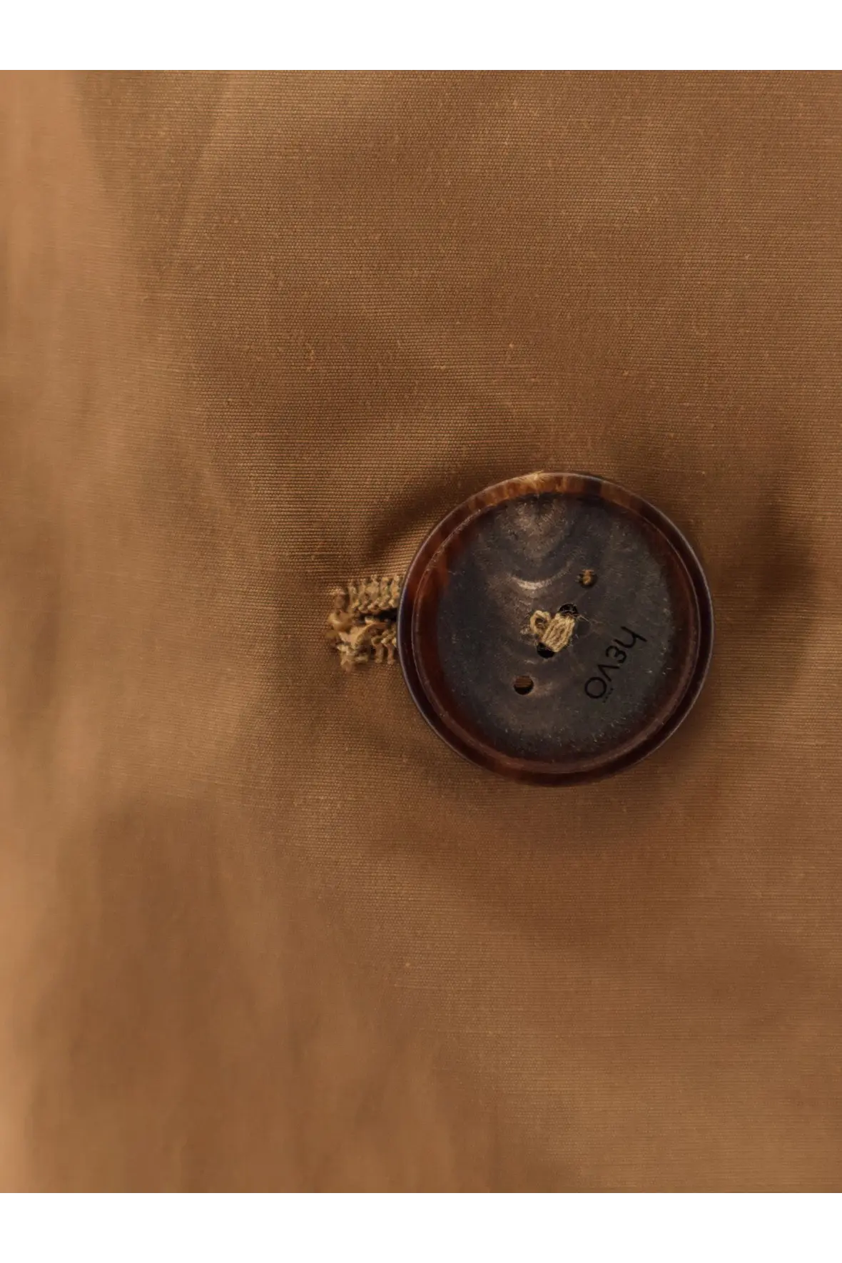 A dark brown textured circular button with two holes on the hevò women’s cala paradiso cotton blend raincoat