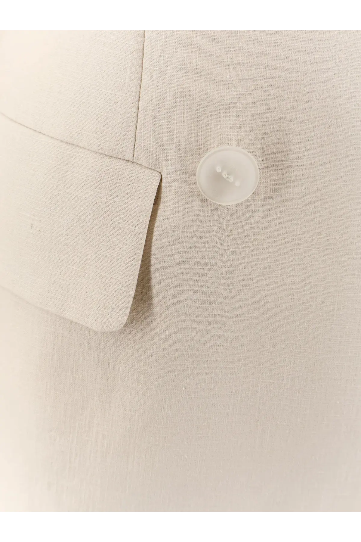 A translucent white button on a textured beige linen and viscose suit from hevò women’s rocchetta collection
