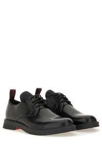 Black patent leather derby shoes with red branding on heel tabs and subtle red sole accent by hugo boss