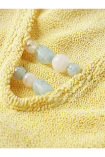 A delicate strand of smooth translucent beads in pastel shades resting on yellow knit fabric with hunza g adriana swimsuit