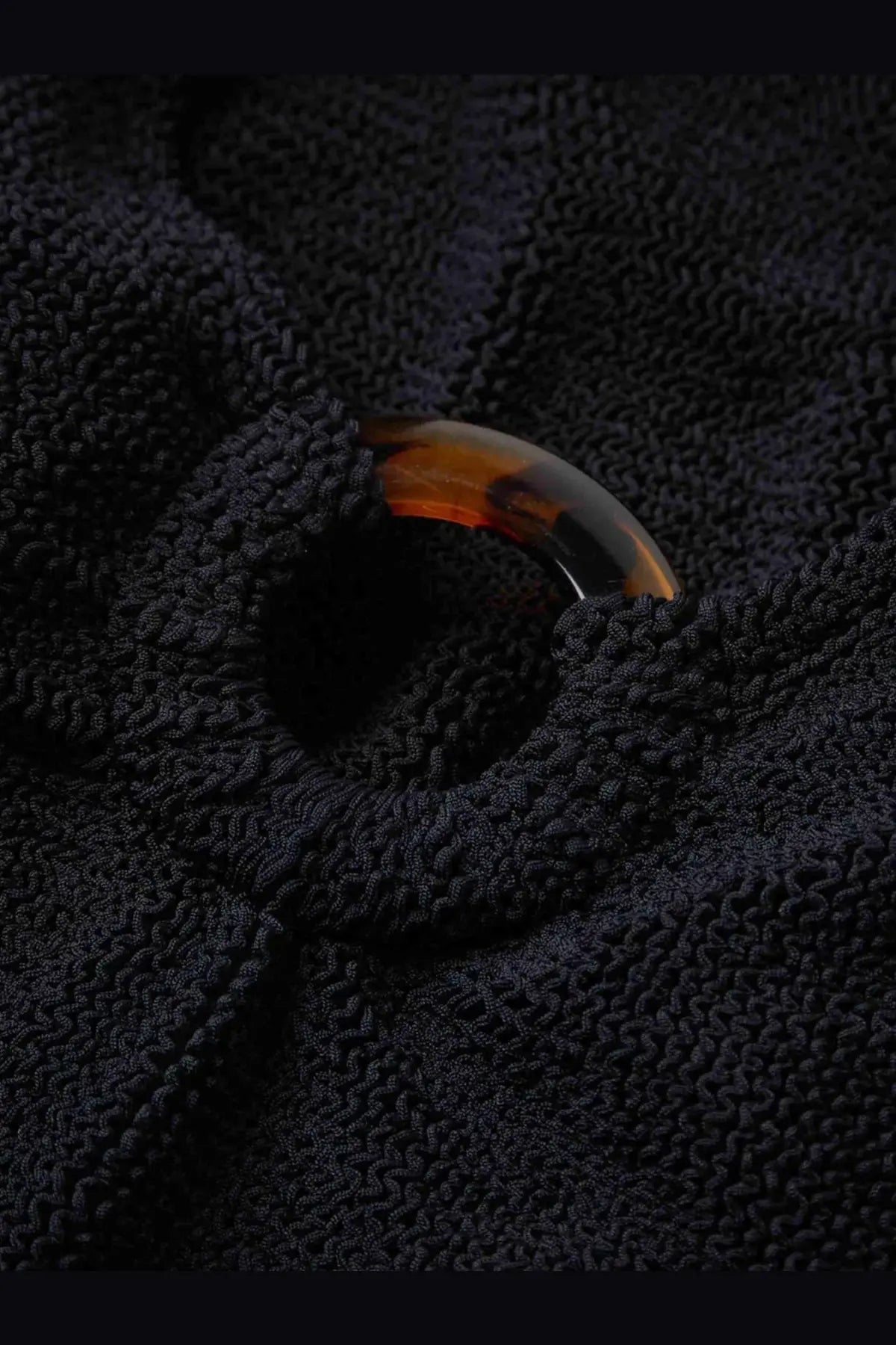 A tortoiseshell curved button with a glossy finish on the textured black crinkle fabric of hunza g womens celine swimsuit