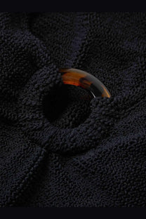 A tortoiseshell curved button with a glossy finish on the textured black crinkle fabric of hunza g womens celine swimsuit