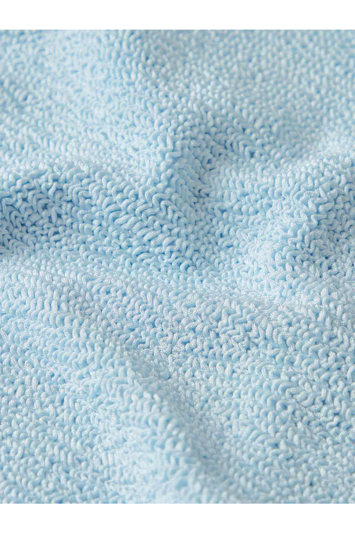 Soft light blue terry cloth towel with plush texture shown alongside Hunza G women’s crinkle fabric one piece swimsuit blue