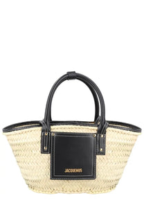 Beige woven straw tote bag with black leather handles and jacquemus logo patch in gold lettering