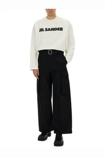 White jil sander long sleeve crewneck sweatshirt with bold black lettering across the chest paired with black cargo pants