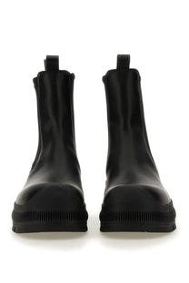 Black patent leather jil sander men’s chelsea boots with chunky rubber sole and pull tabs shown from the back side