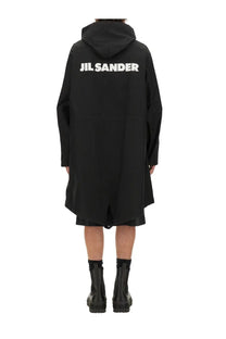 Back side of a black jil sander men’s parka hooded coat with bold white lettering across the back