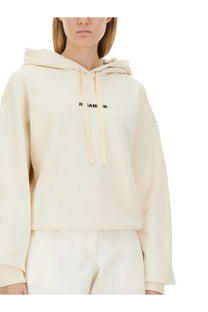 Cream-colored jil sander women’s cropped hoodie with black text across the chest and matching drawstrings
