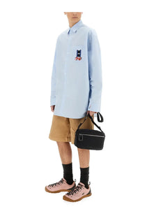 Black crossbody bag with silver zipper and circular logo detail complementing jw anderson men’s blue window shirt