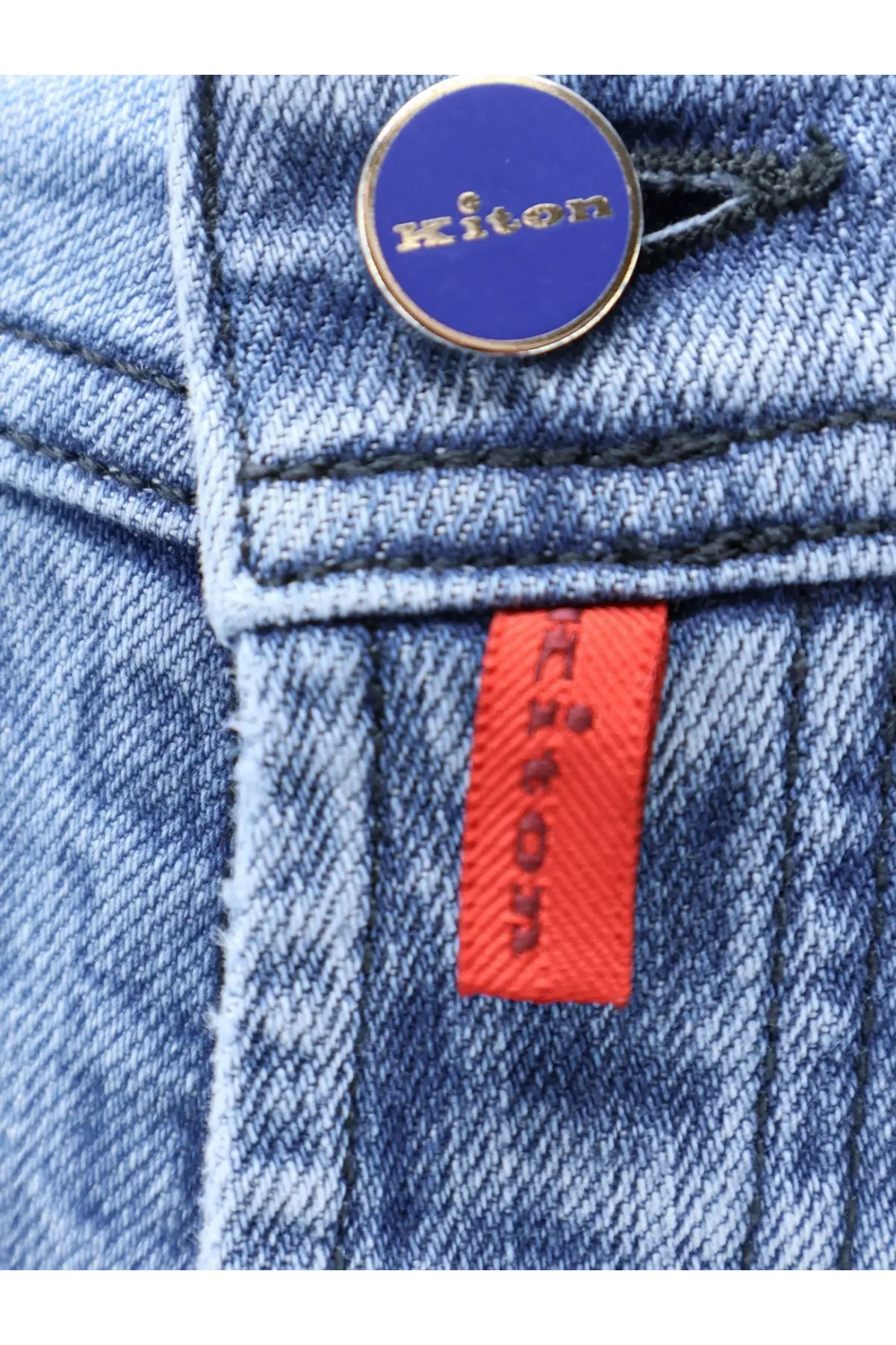 Kiton men’s blue denim jeans with a circular blue and gold Kiton button and an orange brand tag on the front waistband