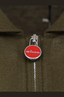 Red circular kiton zipper pull with silver trim and white brand lettering on kiton men’s green cotton polo shirt