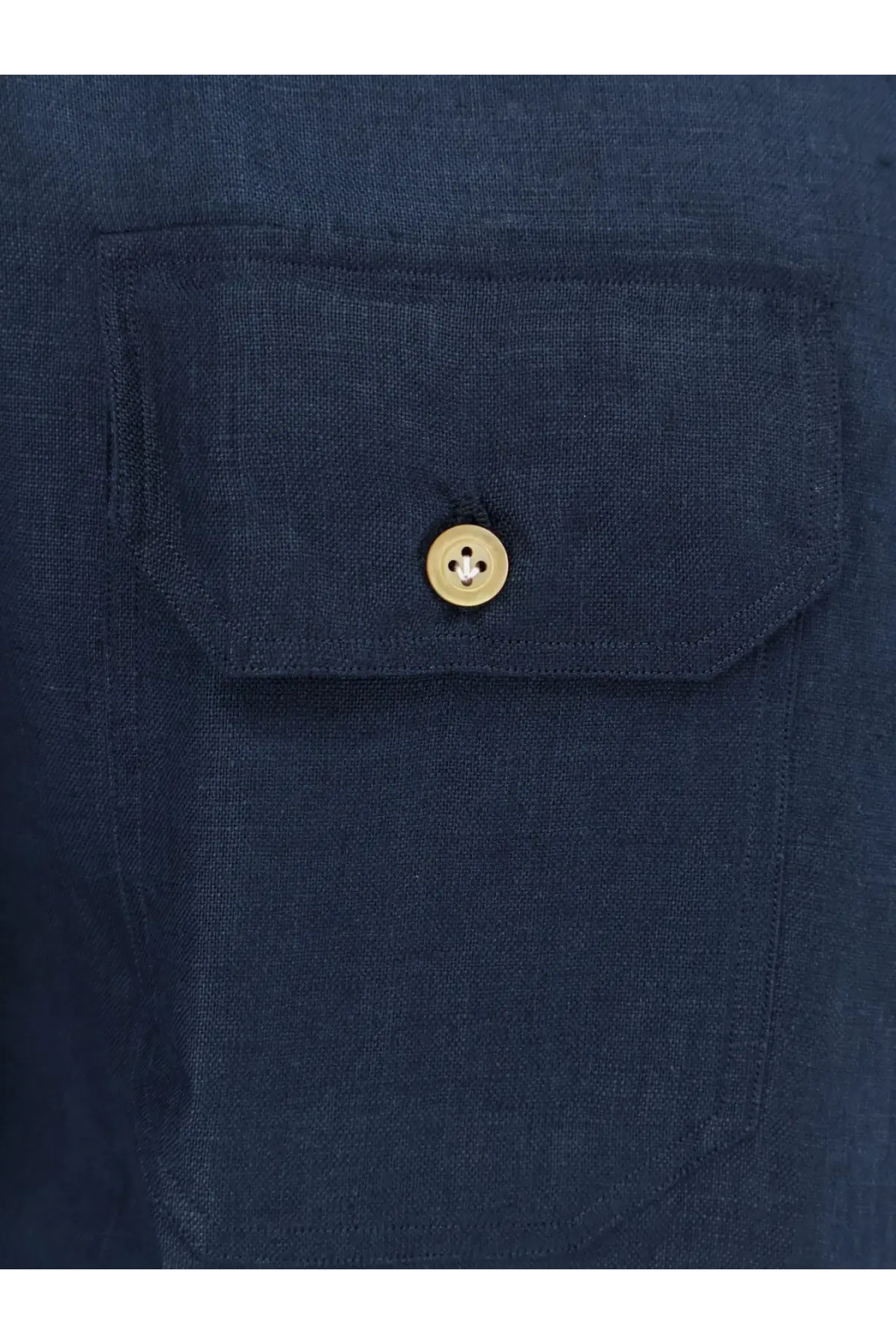 A gold-toned button with four holes on the flap of a dark blue linen kiton men’s shirt pocket