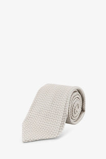 A neatly rolled beige Kiton men’s silk tie with a subtle woven texture and multicolor design