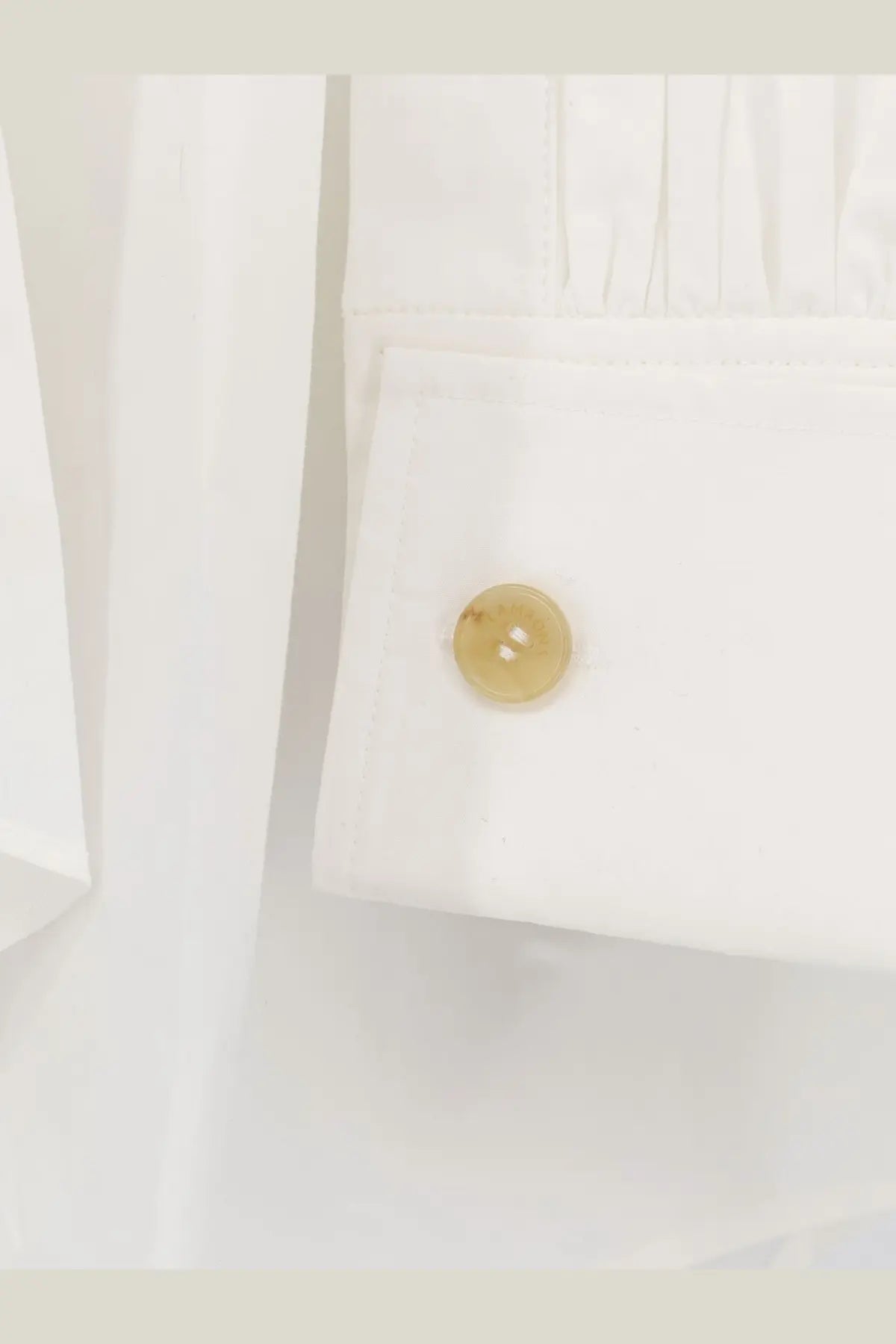 A translucent amber button on the cuff of a crisp white Lamrons women’s cotton shirt