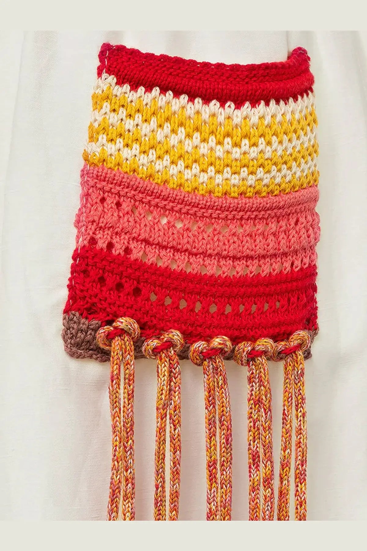 A hand-knitted multicolored fringe pouch in vibrant reds yellows and pinks paired with laneus womens viscose and linen blend cancel bermuda shorts white