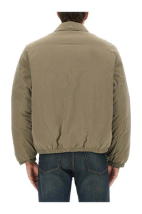 Our Legacy men’s Avenue Smurf jacket green is a khaki puffer jacket with elastic cuffs hem and a subtle collar logo