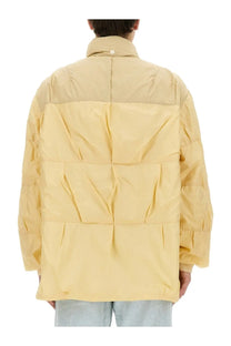 Our Legacy men’s nylon jacket beige features a pale yellow quilted puffer design with a high collar and segmented panels