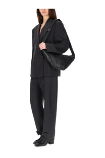 Black quilted leather shoulder bag with structured padded design and long strap paired with lemaire women’s tailored grey pants