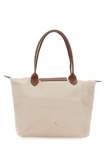 Beige longchamp women’s borsa le pliage medium tote bag with brown leather handles and trim in white background