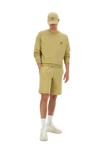A man wearing a beige Maison Kitsuné men’s oversize sweatshirt with embroidered tiger logo, matching shorts, and white sneakers