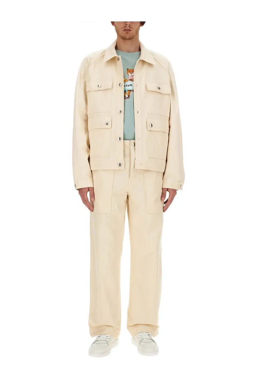 Cream-colored cotton canvas work jacket with flap pockets and button closures shown with maison kitsuné men’s workwear pants white