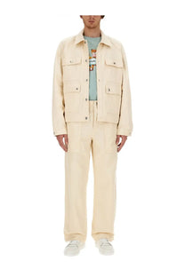 Cream-colored cotton canvas work jacket with flap pockets and button closures shown with maison kitsuné men’s workwear pants white