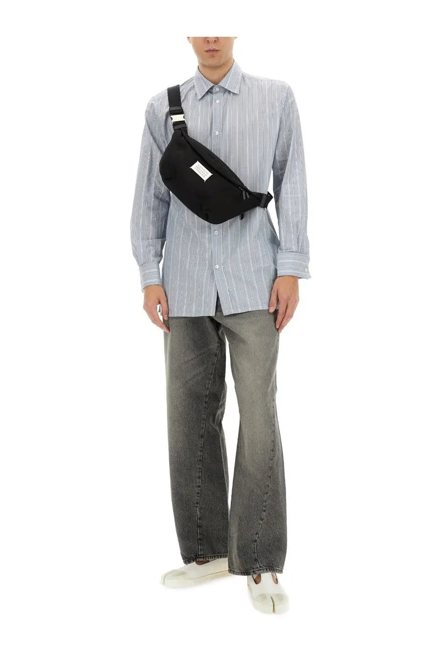 Black canvas waist bag with a white label on the front paired with maison margiela men’s blue striped shirt