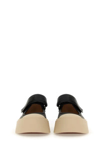 Black leather platform shoes with a beige rubber sole and velcro strap closure.