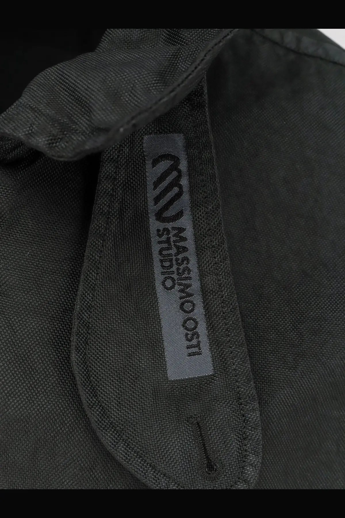 Dark gray textured fabric collar with silver massimo osti studio label on men’s nylon jacket darkshadow