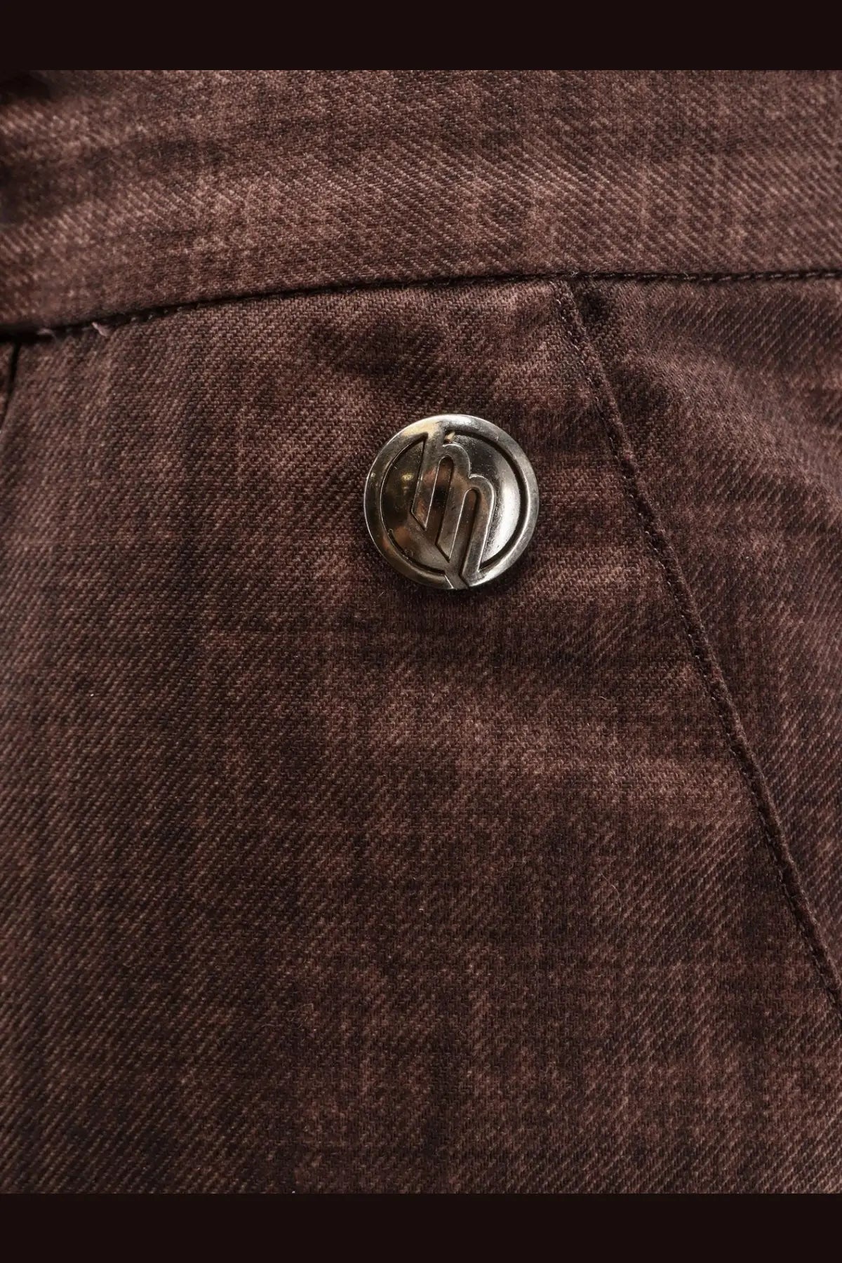 Silver circular button with stylized logo on dark brown denim fabric of massimo osti men’s wool gum trousers brown