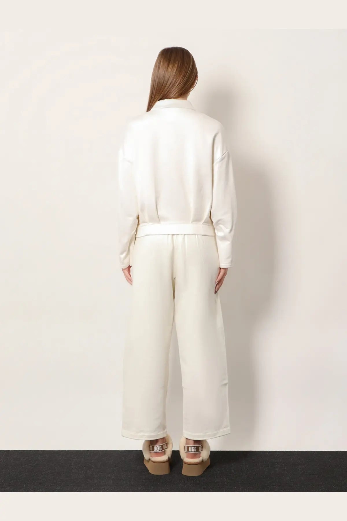 A woman wears a sleek off-white satin jumpsuit with wide-leg trousers and a belted waist