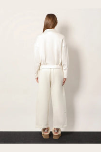 A woman wears a sleek off-white satin jumpsuit with wide-leg trousers and a belted waist