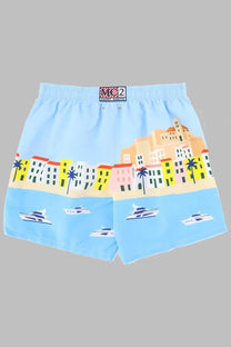 Light blue mc2 saint barth men’s swim trunks with colorful cartoon coastal town print featuring palm trees and yachts