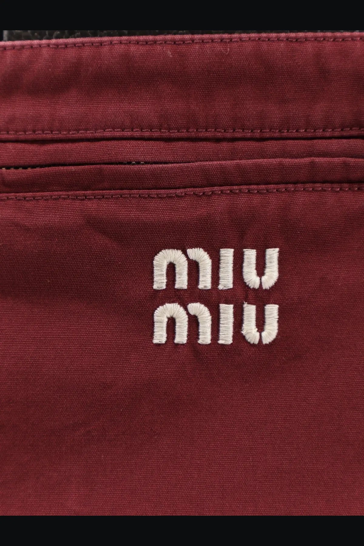 A burgundy canvas crossbody bag with white embroidered miu miu logo paired with a red cotton mini skirt