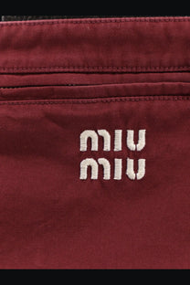 A burgundy canvas crossbody bag with white embroidered miu miu logo paired with a red cotton mini skirt