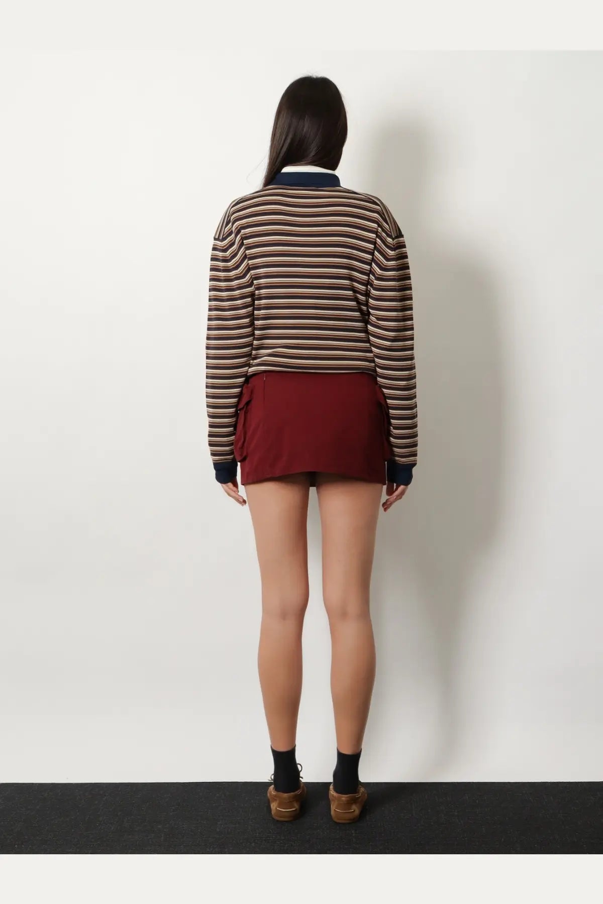 A woman wears a brown and beige striped cotton rugby sweater with navy trim paired with a red Miu Miu cotton mini skirt
