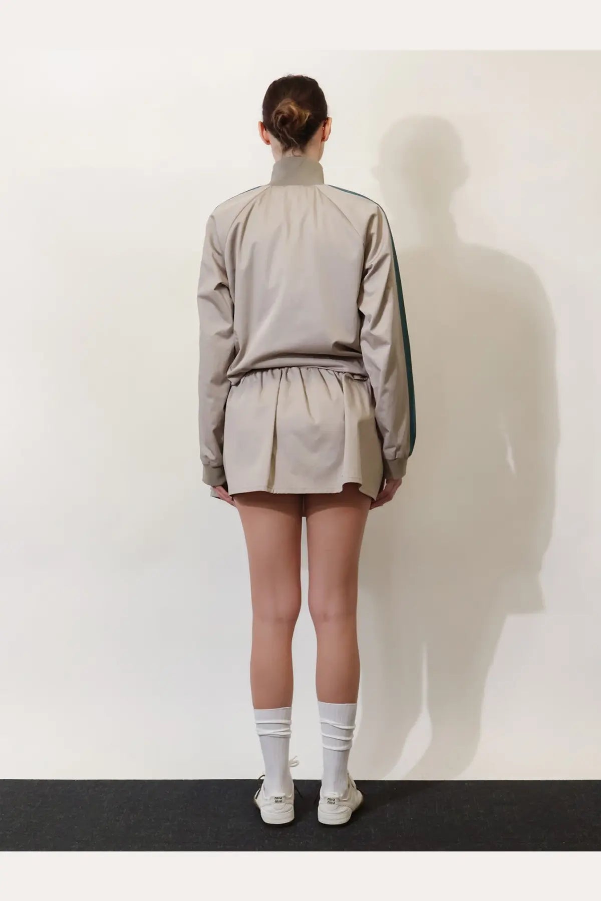 A beige track jacket with a high collar green side stripes and drawstring waistband alongside a miu miu women’s old twill mini skirt green