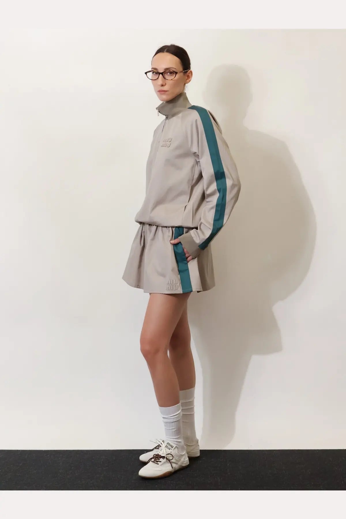 A gray athletic tracksuit set with teal stripes and high collar featuring subtle brand embroidery and matching skirt