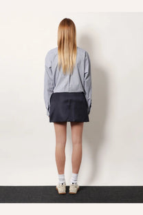 A woman wears a dark navy miu miu mini skirt made from recycled material paired with a blue and white striped shirt