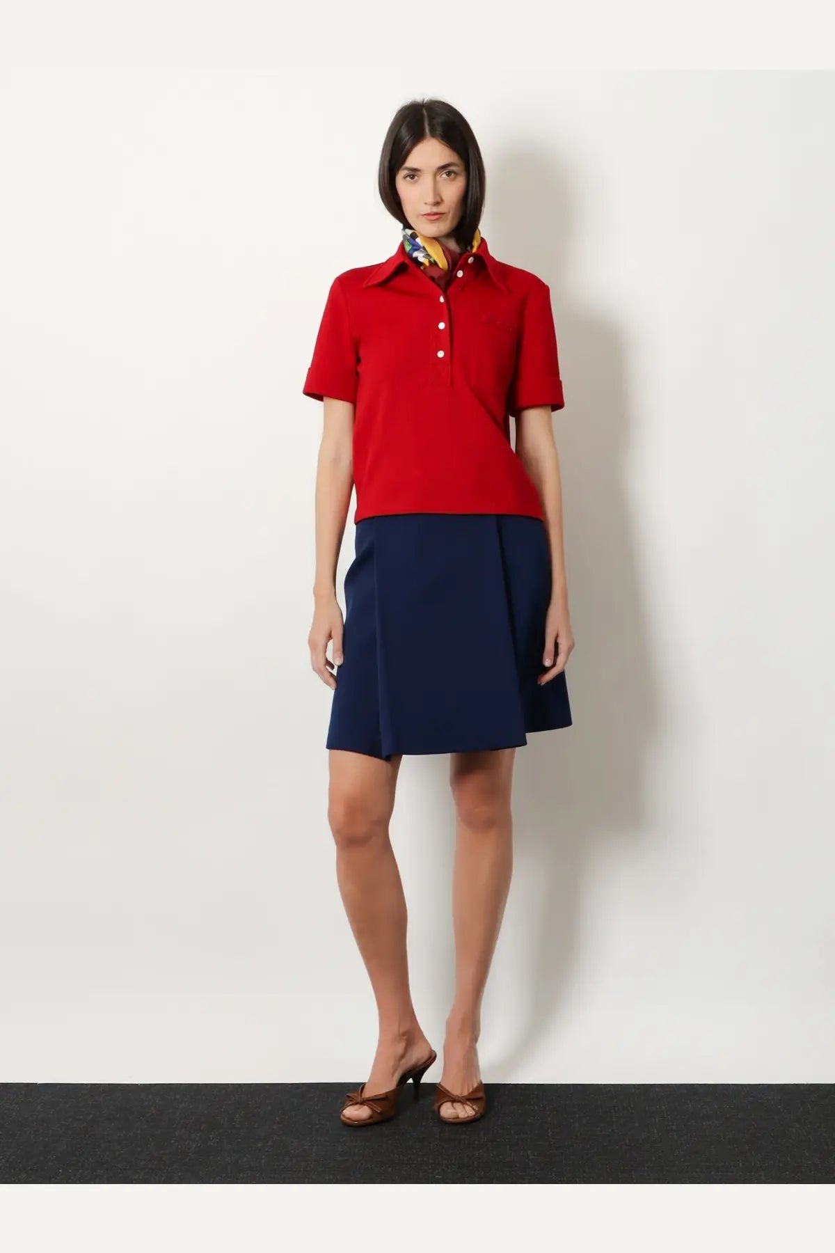 Miu Miu women’s skirt baltico shown with a red short-sleeved polo shirt with white buttons and a colorful patterned collar