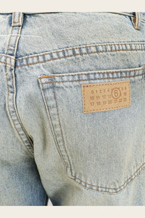Light-wash denim jeans with a tan leather patch stitched with numbers and a number 6 circle by mm6 maison margiela