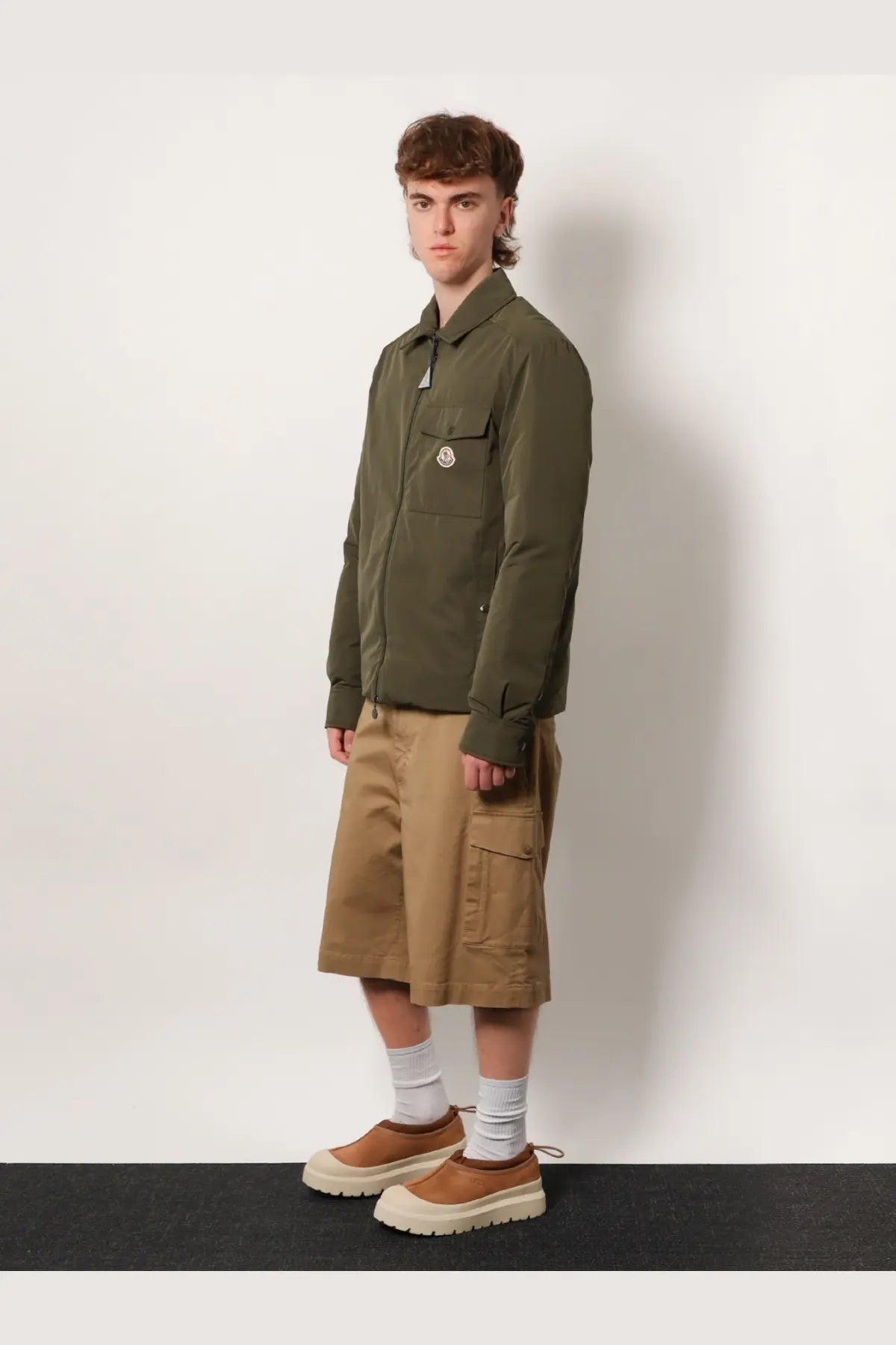 Olive green Moncler men’s jacket with buttoned collar and logo chest pocket paired with beige cargo cotton shorts