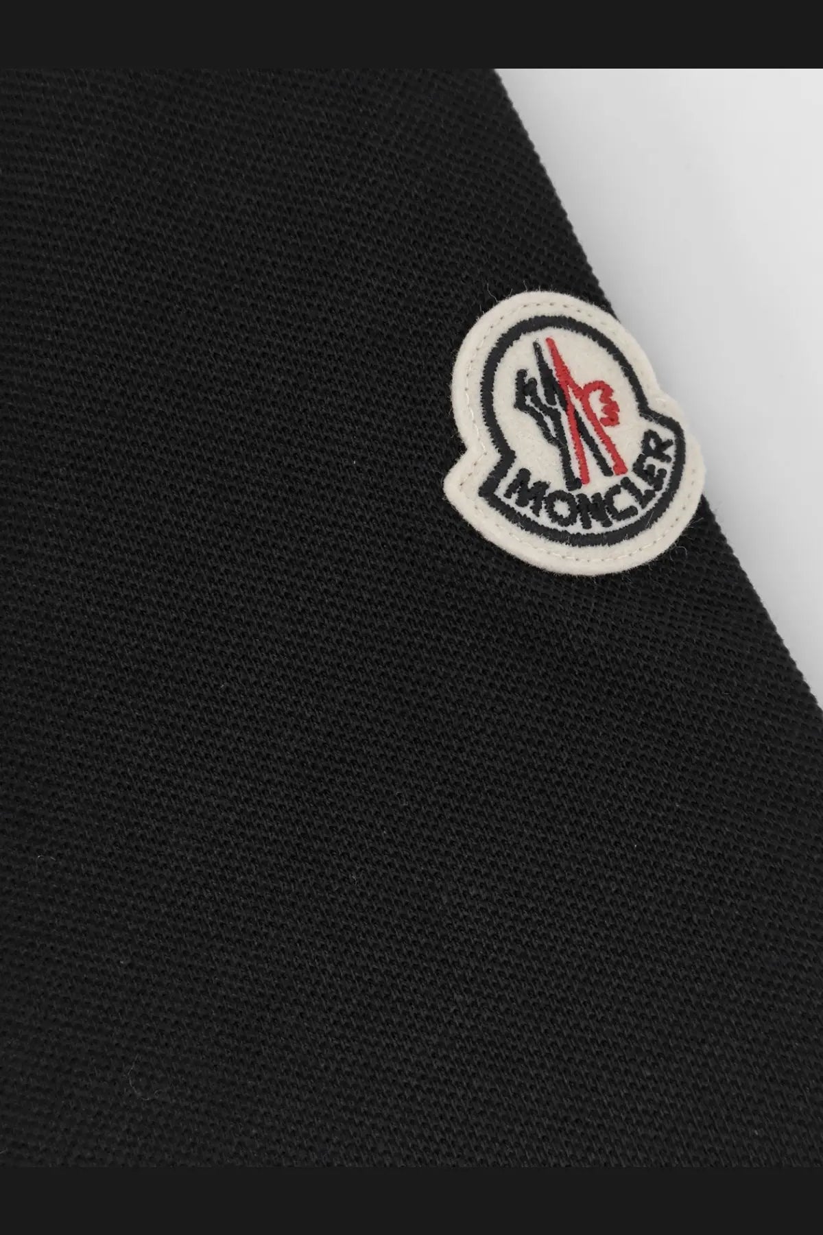 Black moncler logo patch with white border and red embroidered emblem on men’s cotton polo shirt fabric