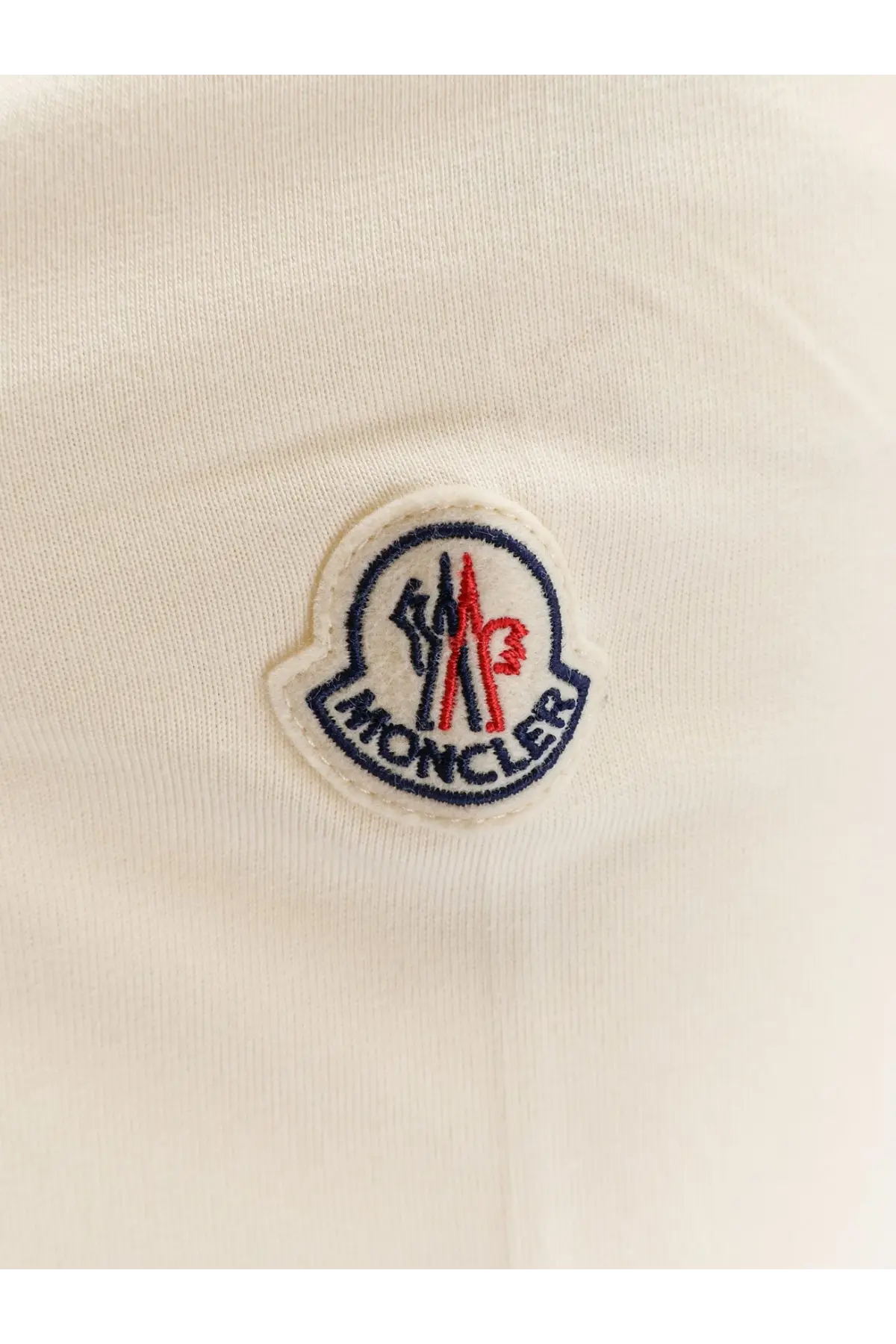 Cream-colored moncler logo patch with embroidered red blue and white details on moncler men’s white cotton shirt