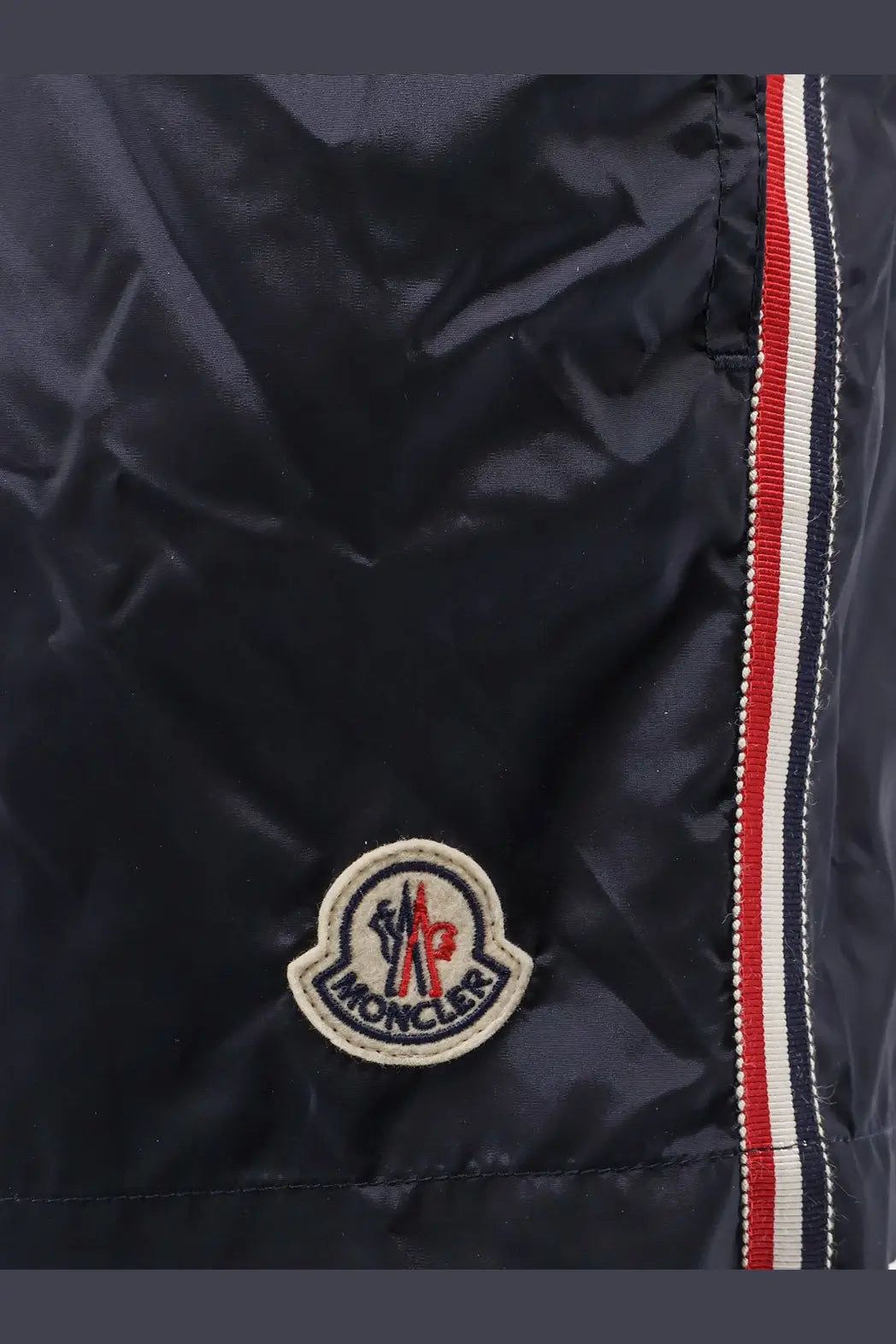 Dark navy moncler jacket with circular embroidered logo and red white and blue striped seam on the back side