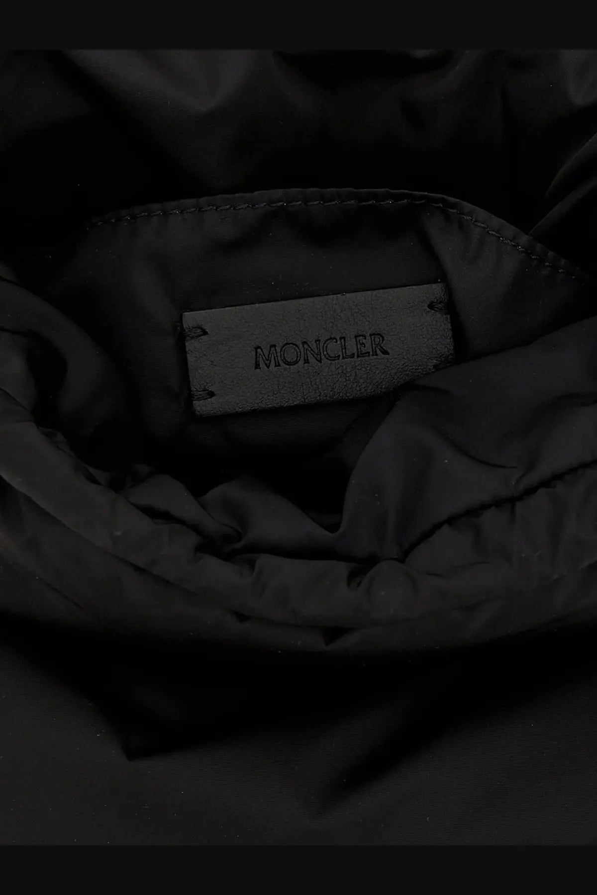 Black moncler brand label stitched into the interior lining of a dark nylon jacket for moncler women’s caradoc bag white