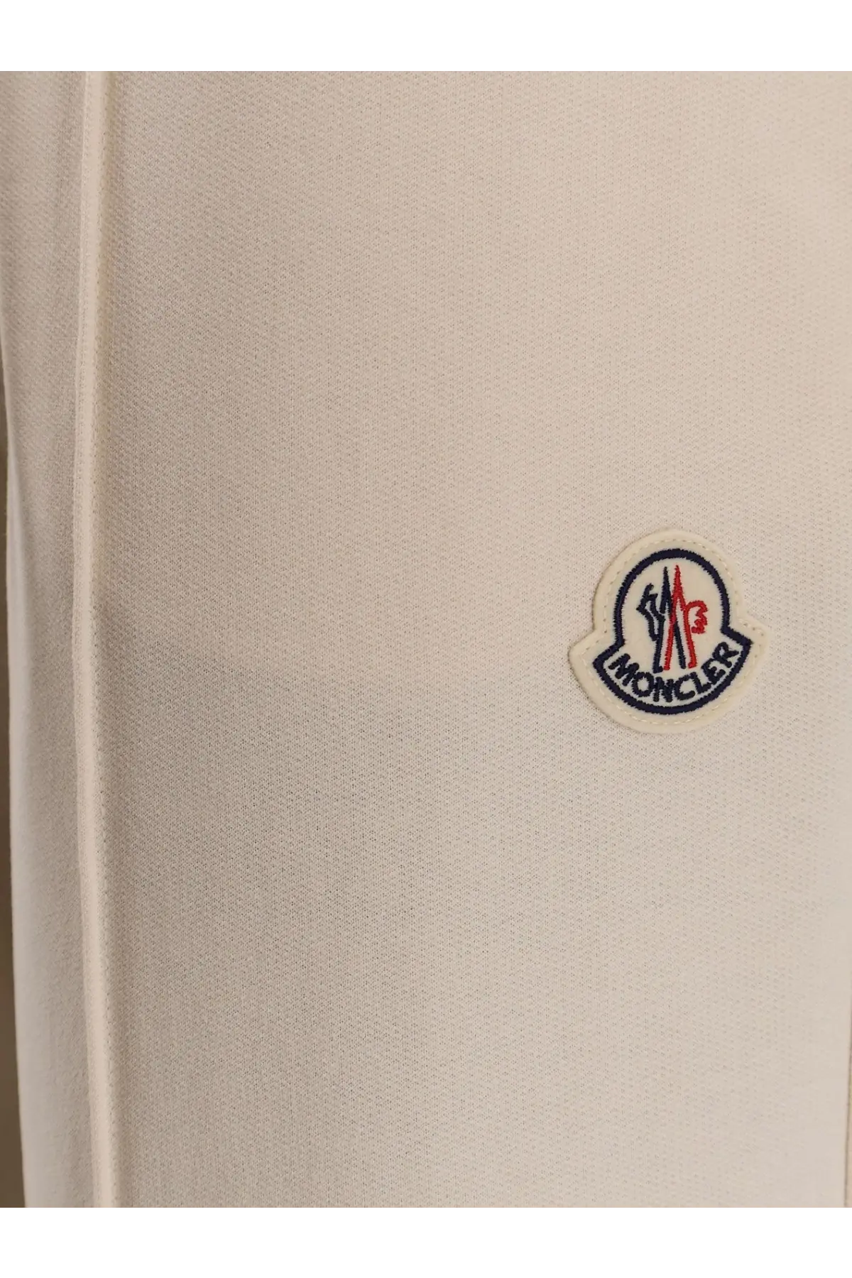 Cream-colored moncler logo patch with red blue and white embroidery on textured fabric of women’s white cotton jogging trousers
