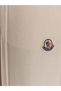 Cream-colored moncler logo patch with red blue and white embroidery on textured fabric of women’s white cotton jogging trousers