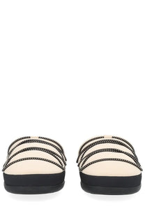 Cream-colored moon boot women’s soft slipper slide sandals with black studded straps and thick flat black sole